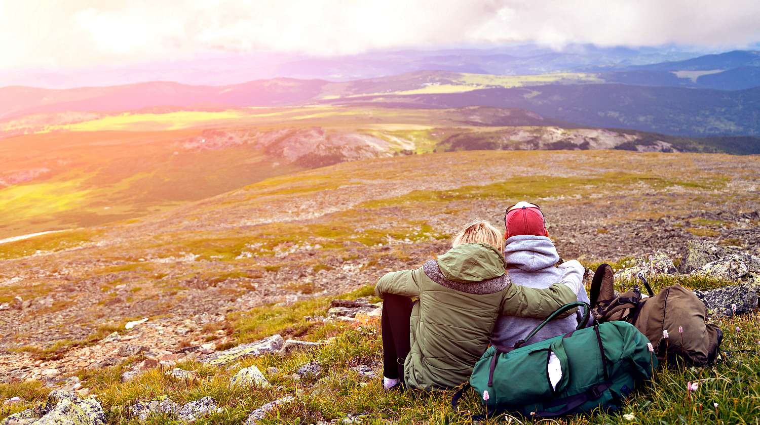Featured | Hiking lovers with backpack is sitting on the top of the mounting and looking at a beautiful landscape | Survivalist Dating Sites: Seeking A friend For The End Of The World