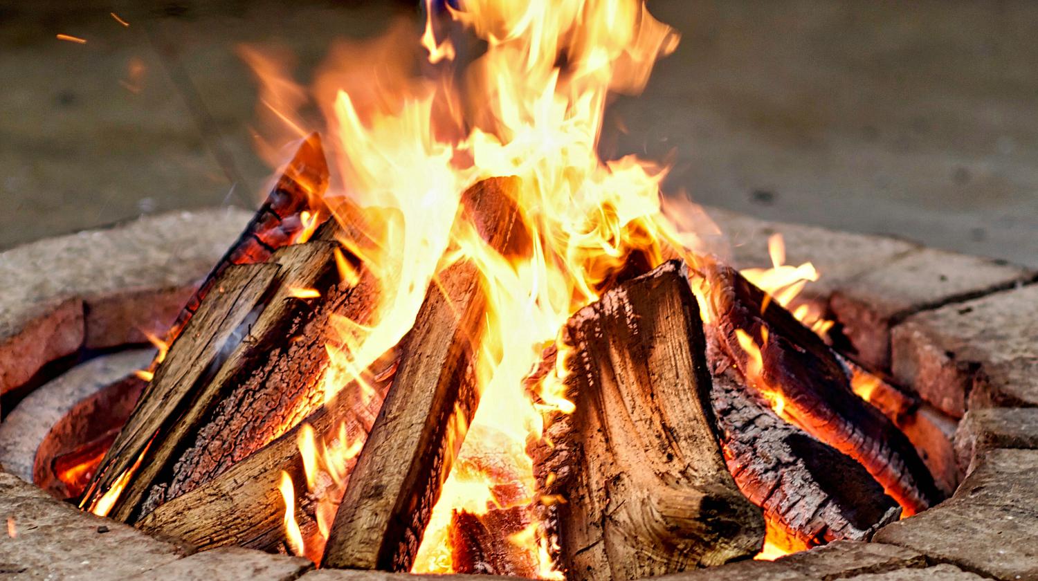 Close-up, roaring fire with blurred flames from wood logs in a stone firepit | How To Build A Fire Pit | Featured