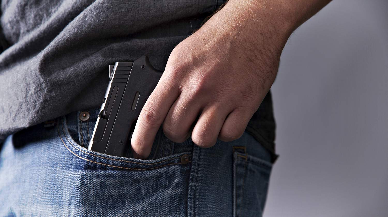 A man legally carries a firearm in his pocket for protection close up | Concealed Carry Tips | Traveling With A Gun | Featured