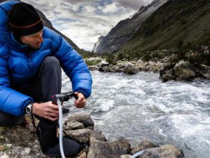 A man in blue down jacket filtering water for drinking from a river | How To Make A DIY Pocket Water Filter [Video] | Featured