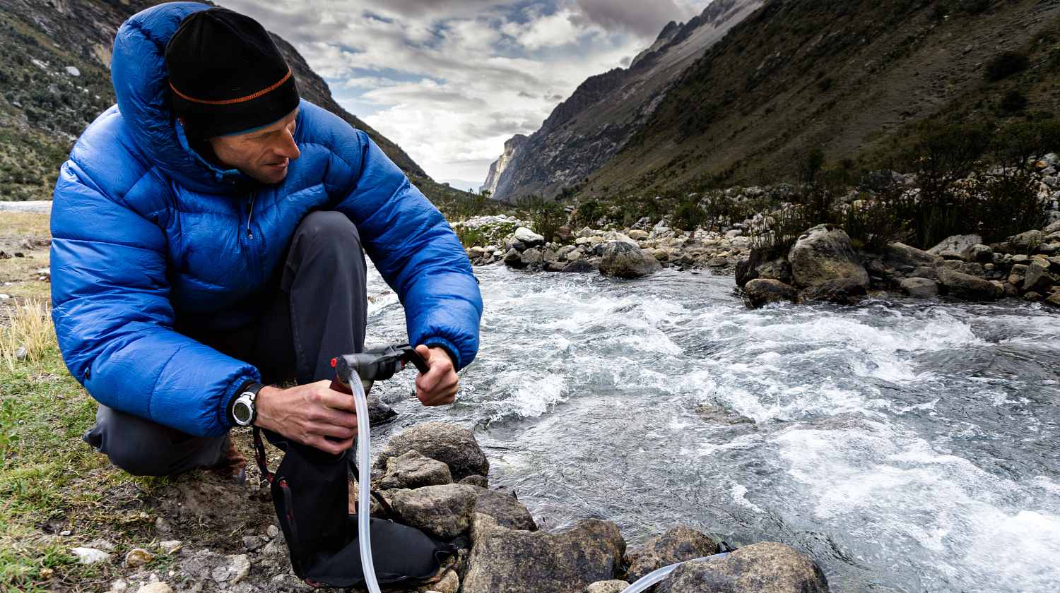 A man in blue down jacket filtering water for drinking from a river | How To Make A DIY Pocket Water Filter [Video] | Featured