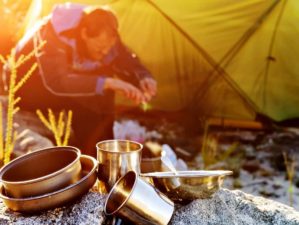 Featured | Adventure camping man cooking alone outdoors with tent, sunrise and lens flare in the mountain morning sunlight | Outdoor Survival Hacks Using Everyday Items