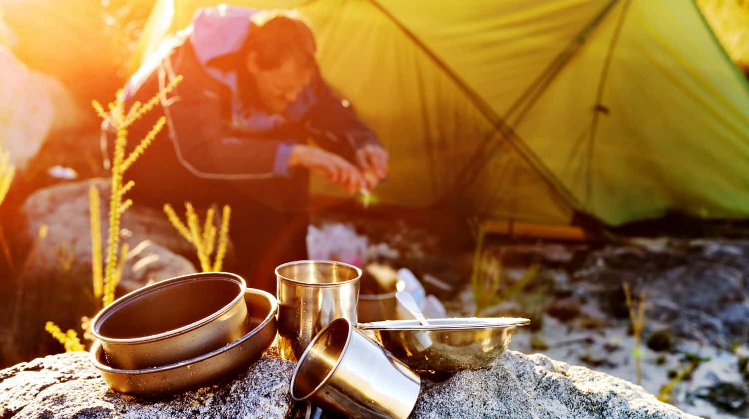 Featured | Adventure camping man cooking alone outdoors with tent, sunrise and lens flare in the mountain morning sunlight | Outdoor Survival Hacks Using Everyday Items