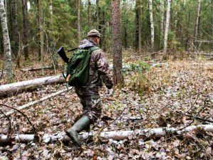 Man the hunter goes through the forest in rubber boots, with a backpack and a gun | Go Bag Guns | Getting Your Firearms In Order When SHTF | Featured