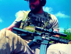 Feature | man sitting on the ground carrying a rifle | Everything You Need To Know About The AR15 Rifle Platform | ar15 history