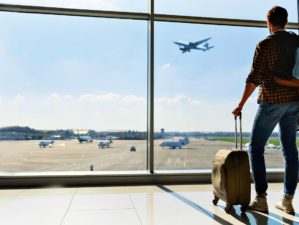 Feature | Young man is standing near window at the airport and watching plane before departure | Travel Safety Tips You Shouldn't Ignore