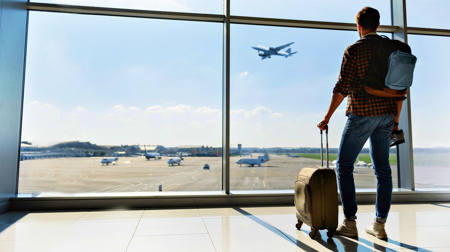 Feature | Young man is standing near window at the airport and watching plane before departure | Travel Safety Tips You Shouldn't Ignore