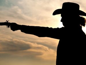 Feature| Silhouette of a young man in a cowboy hat shooting an antique hand gun | Lessons On Gunfighting From Wyatt Earp