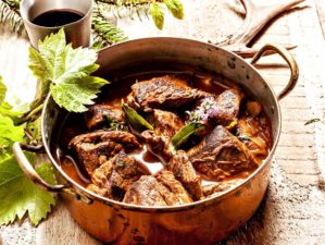 Featured | Venison goulash stew in copper pot with wowls of seasoning on wooden surface | Unconventional Venison Recipes To Try This Hunting Season