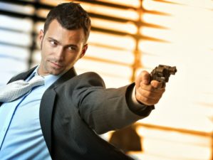 Feature | Determined caucasian action hero wearing suit and tie holding gun in hand | Great Action Movie Gun Quotes That Apply To EDC