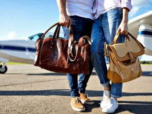 Young couple carrying brown leather bags at air plane on runway | Airport Go Bag | Must-Have Items For The Prepared Traveler | Featured