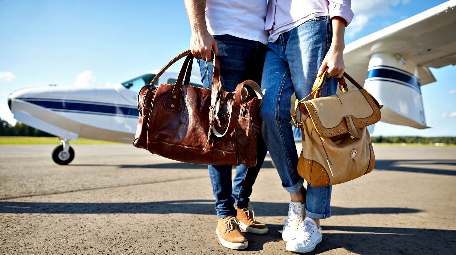 Young couple carrying brown leather bags at air plane on runway | Airport Go Bag | Must-Have Items For The Prepared Traveler | Featured