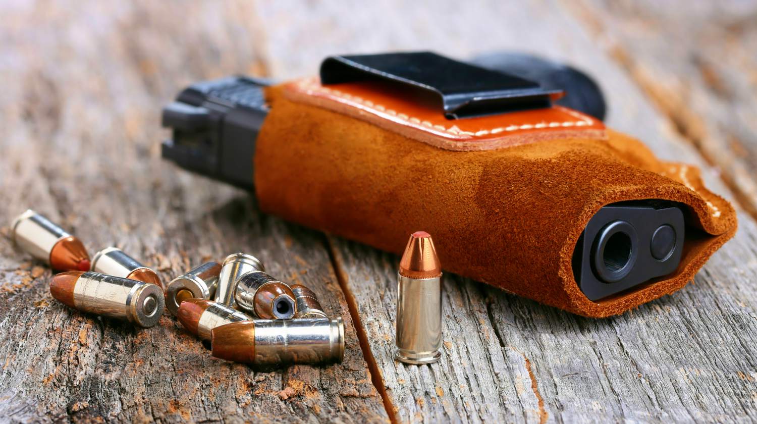 Featured | Automatic Handgun with leather holster and bullets on a wooden background | Gear Review: Urban Carry Holster, Yay Or Nay?