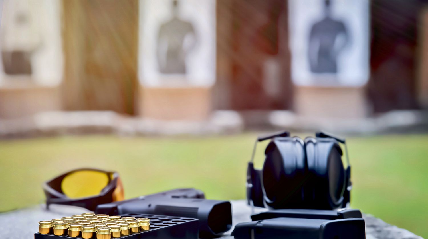 Feature | Gun, bullets, ear plugs and shooting accessories on the table at shooting range | Shooting Fundamentals