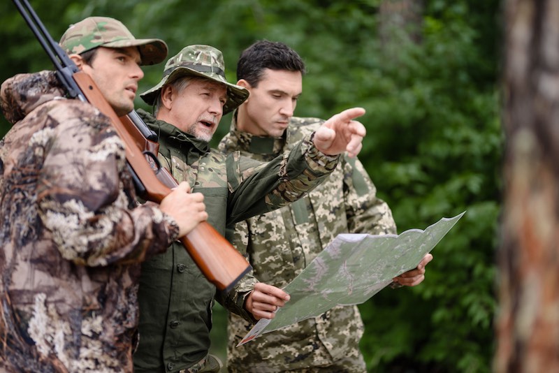 Hunters stand and discuss the road in the forest. Hunters in equipment with guns stand in the wild forest. | how to get into hunting reddit