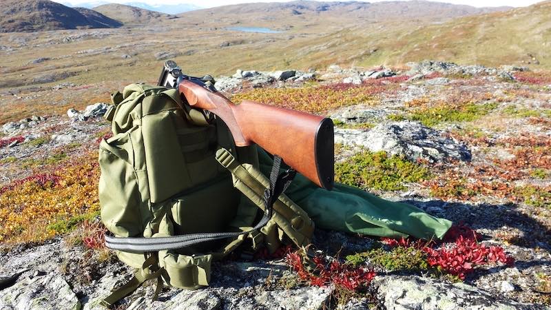 shotgun resting on green backpack with freshly hunted grouse birds in hunting net bag | whitetail hunting checklist
