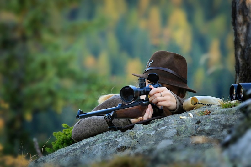 Young, Clever Woman Deer Hunter wearing green uniform with Rifle | muzzleloader brands