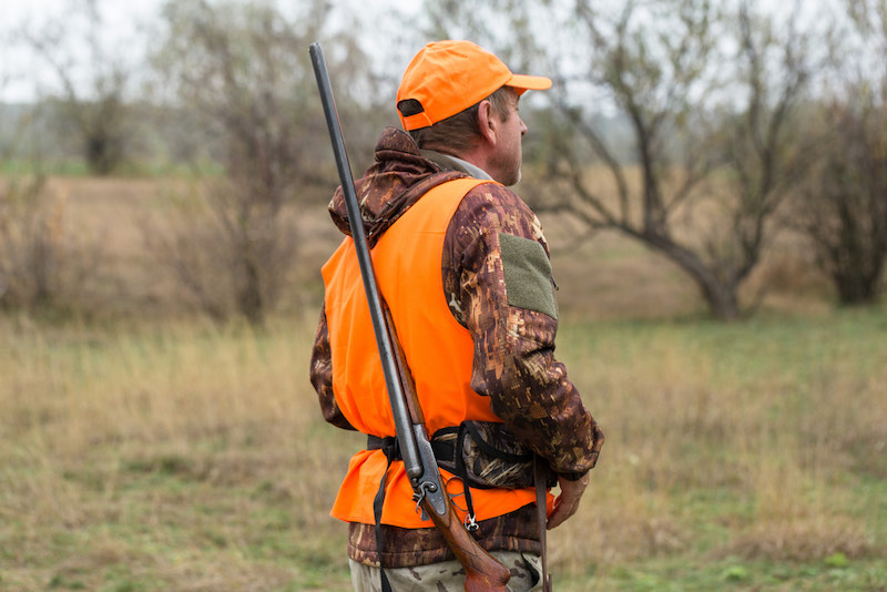A man with a gun in his hands and an orange vest | essentials for deer hunting