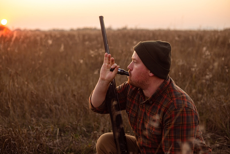 Young red bearded hunter sitting it grass and blowing at hunter's whistle | california pheasant hunting clubs
