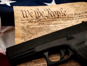 The second amendment and gun control in america concept with a handgun and the american constitution on the USA flag with close up on the we the people-Second Amendment Sanctuary-ss-featured