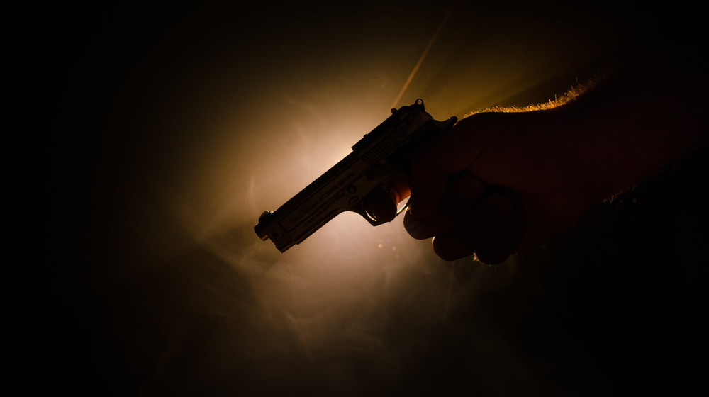 Male hand holding gun on black background with smoke | Best Pistol Lights And How To Choose Which One Is Right For You | featured