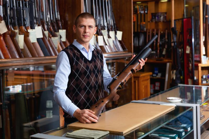 Gun shop salesman standing behind counter and showing modern sporting air PCP pump action rifle | airgun