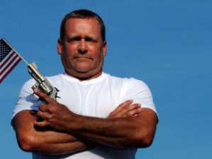 Muscular White Man Holding An American Flag And Gun, symbolizing our constitutional right to own and bear arms-Gun Owner-ss-featured