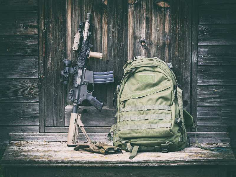 Tactical carbine and green backpack on the steps of the old house-Essential Guns