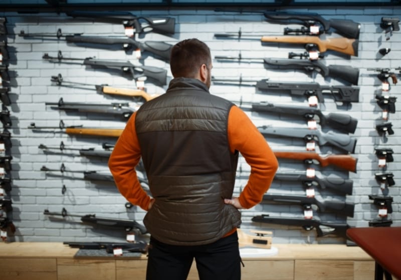 Man at showcase with rifles, back view, gun shop | pump shotgun