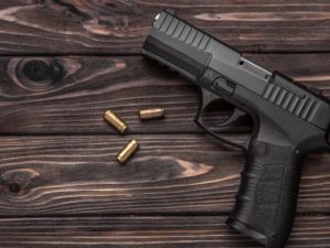 Black pistol and cartridges on a brown wooden background | Top 10 Best Performing Pistols for 2021 | Featured